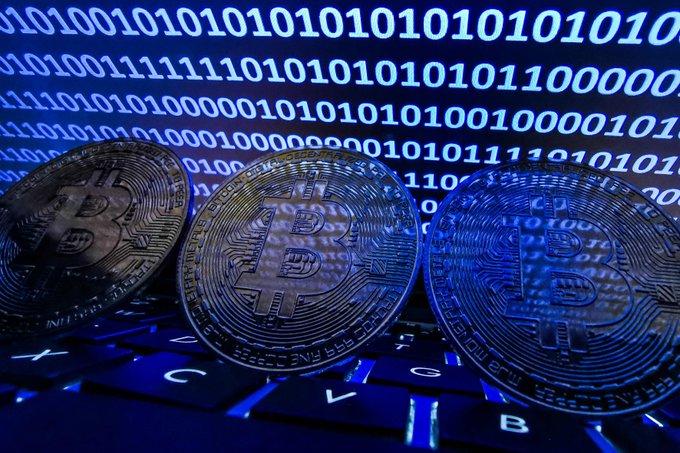 Three physical Bitcoin tokens rest on a backlit keyboard in front of a screen displaying streams of binary code, visually symbolizing the digital cryptocurrency assets at risk in the reported Coldcard hardware wallet seed generation vulnerability that has led to over 594 BTC (~$40 million USD) being stolen by hackers.