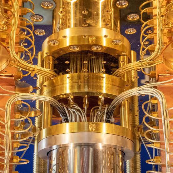 A complex golden mechanical structure, possibly a quantum computer, features multiple cylindrical chambers, intricate wiring, and a highly reflective metallic finish.