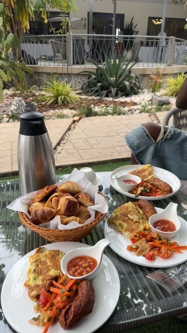 A patio breakfast spread featuring frittatas with beans, roasted potatoes, a vegetable medley, and a basket of croissants next to a thermal carafe.