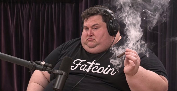A man wearing a 'Fatcoin' t-shirt and headphones holds a smoking cigar in front of a microphone against a dark curtain backdrop.