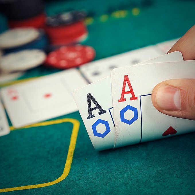 A hand holds three aces over a green felt card table scattered with poker chips, symbolizing high-stakes risk and reward—mirroring the post's message about Chainlink's volatile price swings, where investors must be prepared to win big or lose access to a token quietly powering banks, stablecoins, and SWIFT infrastructure.