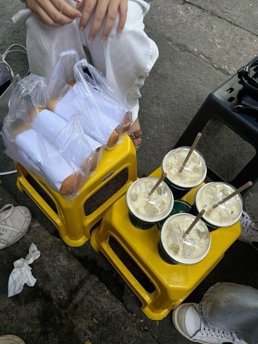 Four iced drinks in plastic cups sit on a yellow plastic stool alongside bags of bread, with a person holding an umbrella above the setup. The image humorously illustrates the post's point about absent repayment expectations—much like casually lending an umbrella without expecting it back, suggesting TermMaxFi offers better lending protocols than everyday informal loans.