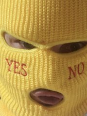 A person wearing a yellow balaclava with the words 'YES' and 'NO' printed over the mouth area.