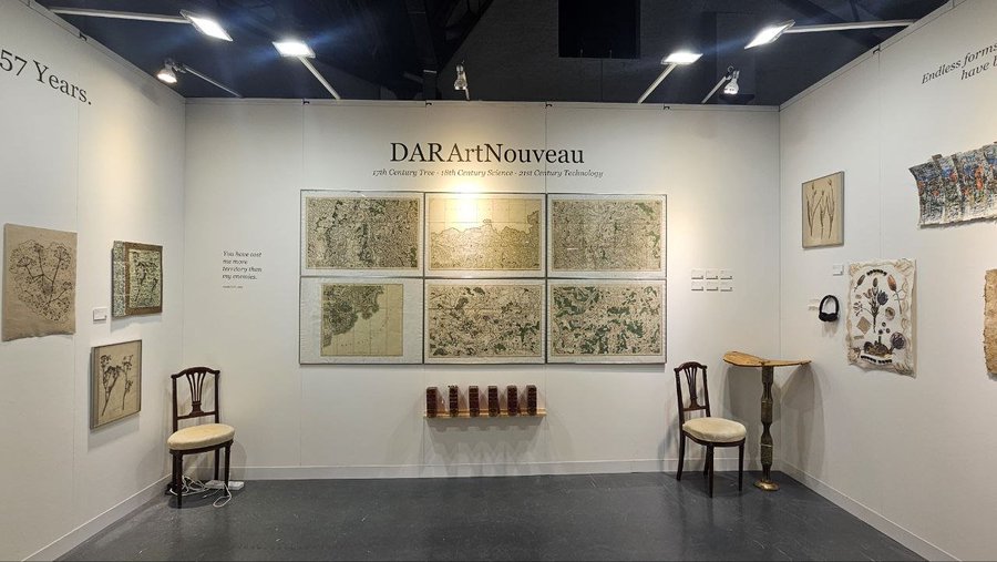 An art gallery exhibition booth titled 'DARArtNouveau' displays six framed maps along the center wall, flanked by framed sketches on the side walls, with two chairs and a small table in the foreground. Text on the walls reads '57 Years.', 'Endless forms... have b...', and '17th Century Tree - 19th Century Science - 21st Century Technology'.
