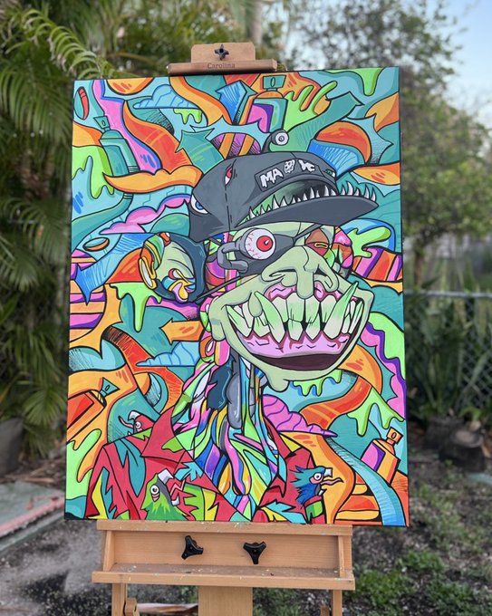 A vibrant, graffiti-style painting on a canvas resting on a wooden easel outdoors, depicting a green monstrous face with sharp teeth and a hat, surrounded by colorful abstract shapes, fish, and bottles.
