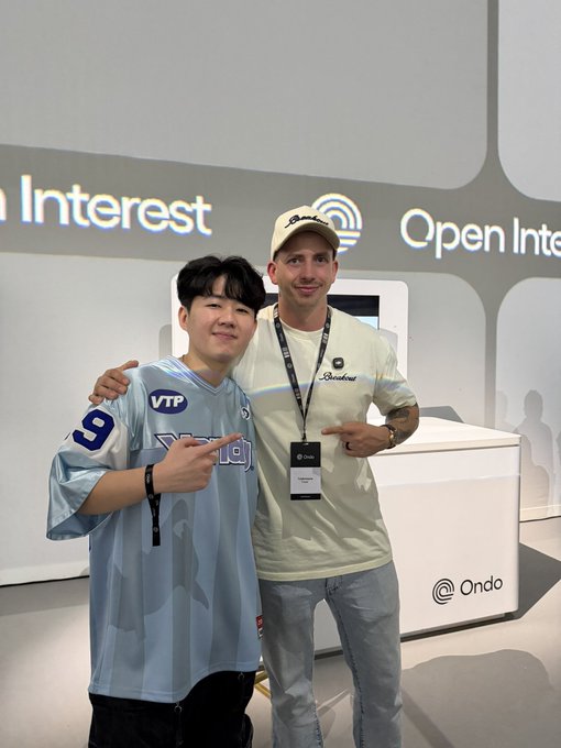 Two men smile and pose together at the "Open Interest" event hosted by Ondo, with visible signage for "Open Interest" and "Ondo" branding behind them, capturing the networking highlight of Token2049 mentioned in the caption.