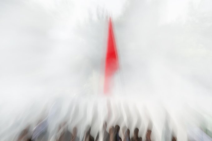 A heavily motion-blurred image showing what appears to be a crowd of people with a red vertical streak in the center against a white background.
