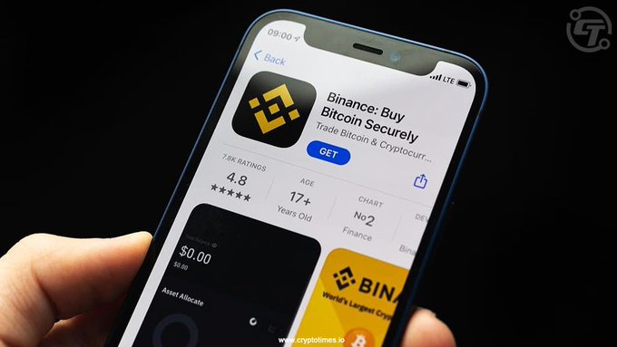 A hand holding a smartphone displaying the App Store page for the 'Binance: Buy Bitcoin Securely' app with a 4.8 rating.