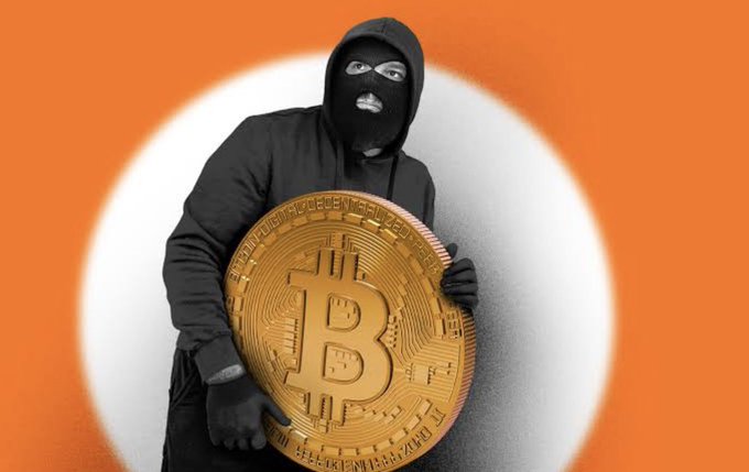 A person wearing a black hoodie and ski mask holds a large gold Bitcoin coin against an orange background with a white circular spotlight effect.