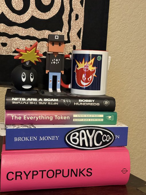 The image features a stack of books, with one book prominently displaying the words "Cryptopunks" written on its cover. This book seems to be part of a collection or display related to Cryptopunks. The other books are arranged in a way that they appear to be stacked together, creating an interesting visual effect.