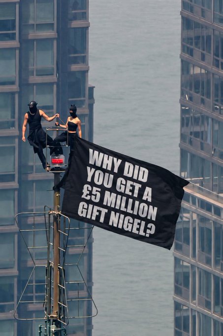 Two protesters, dressed in black and wearing black face masks, perch atop a tall pole between skyscrapers while unfurling a banner reading "WHY DID YOU GET A £5 MILLION GIFT NIGEL?" — a direct question to Nigel Farage matching the post's skepticism about undisclosed political funding.
