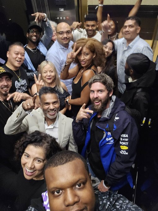 A large group of people take a selfie together at what appears to be an event, with one man wearing a jacket displaying logos for Visa, AT&T, Rokt, and Yoco.