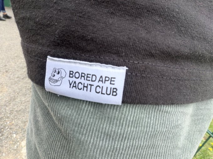 A close-up of a 'BORED APE YACHT CLUB' clothing label with a skull logo sewn onto a dark gray shirt.