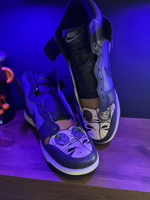 A pair of custom Nike sneakers featuring purple and black colors with an anime face design on the toe box, displayed under blue lighting.