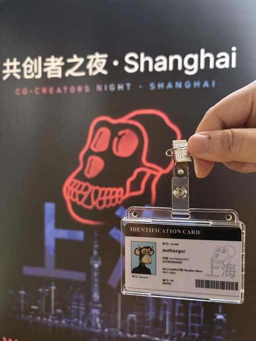 A hand holds up an "IDENTIFICATION CARD" bearing the name "notburger" with the handle "OVERSIDE" and a monkey avatar, against a backdrop for "共创者之夜·Shanghai / CO-CREATORS NIGHT · SHANGHAI" featuring a red skull graphic, highlighting the international gathering of Bored Ape community members in Shanghai.