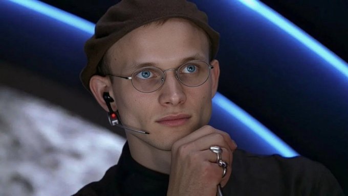 The image features a man wearing glasses, a hat, and a ring with multiple fingers. He seems to be deep in thought or contemplating something as he gazes off into the distance. The surrounding background consists of blue lights that cast an intriguing glow on the scene. The image also contains text elements such as "ETH crashed below $1,500" and "Another $200M dumped my Ethereum," which might suggest a connection to cryptocurrency or an event involving Etherium's value.