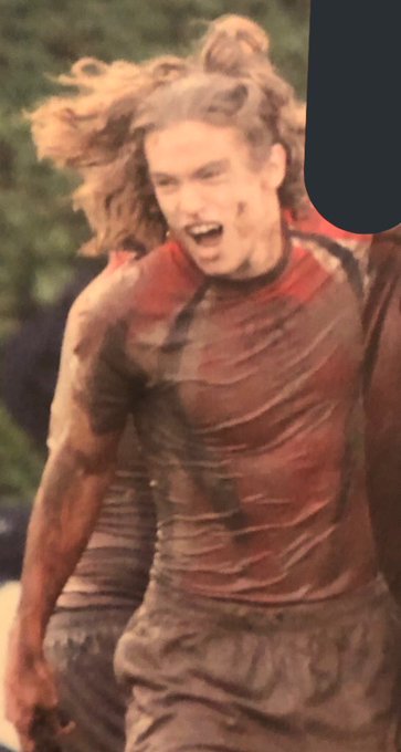 A mud-splattered rugby player with long hair flowing wildly celebrates intensely on the field, embodying the regretful shift from football to rugby described in the post. The dirt-streaked jersey and passionate energy visually capture the pivot the author made after leaving varsity football to play only rugby.