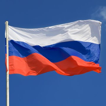 The Russian flag waves against a clear blue sky.