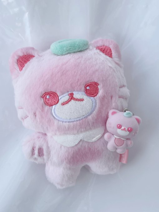 A fluffy pink plush toy character with a small green leaf on its head, accompanied by a matching pink keychain, resting on a white surface.