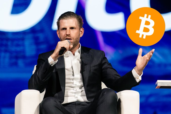 Eric Trump speaks at a conference with a Bitcoin logo displayed in the corner, accompanying news that American Bitcoin has increased its holdings by 300 BTC to reach 8,300 Bitcoin total.