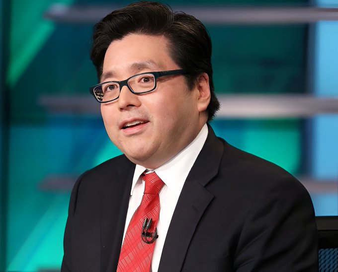A man wearing glasses, a dark suit, white shirt, and red patterned tie speaking on what appears to be a financial news program with a green studio background.