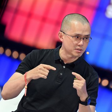 A man with a shaved head and glasses, wearing a black polo shirt, gestures emphatically while speaking at what appears to be a conference or panel discussion, with colorful red and blue lighting in the background.

The image likely depicts Changpeng Zhao (CZ), the former CEO of Binance, making his prediction about Bitcoin surpassing gold's importance in the next bull run.