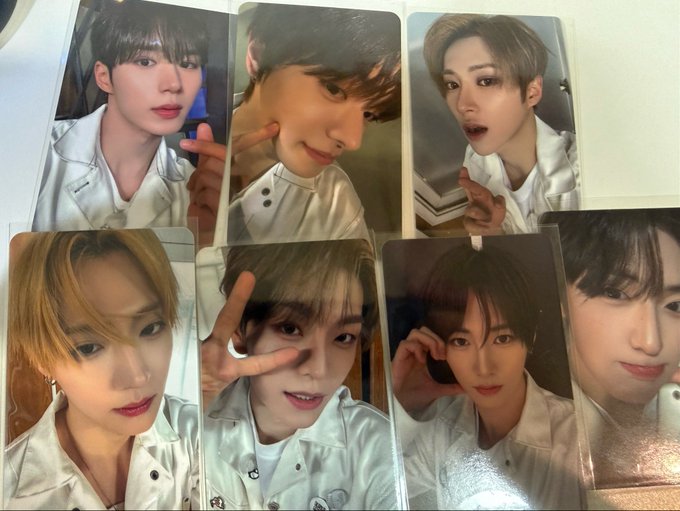 Seven photocards of a K-pop idol with light-colored hair are arranged in two rows, showing him in white outfits making cute poses like peace signs and playful expressions. The post expresses gratitude for receiving these cute photocard gifts, mentioning the group/hashtags ALD1 (Alpha Drive One) and XINLONG.