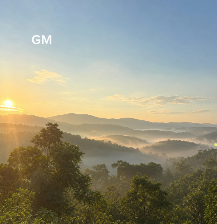 A scenic sunrise over misty mountains and a forested valley, with the text 'GM' overlaid in the upper left.