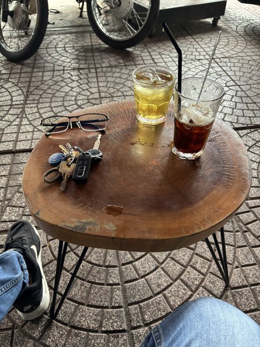 The image shows a wooden table with two glasses of soda, one containing an alcoholic beverage (likely beer) and the other filled with water or another non-alcoholic drink. The table also has a pair of sunglasses placed next to it. A keychain is located on the table as well.
