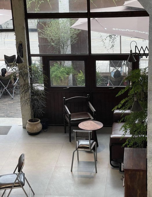 A quiet café interior with empty chairs, a small round table, and large windows looking out onto a patio with a "Stop for Coffee" umbrella, evoking a peaceful morning moment. The serene, inviting setting complements the post's hopeful Friday message of new beginnings and the promise of the weekend just around the corner.