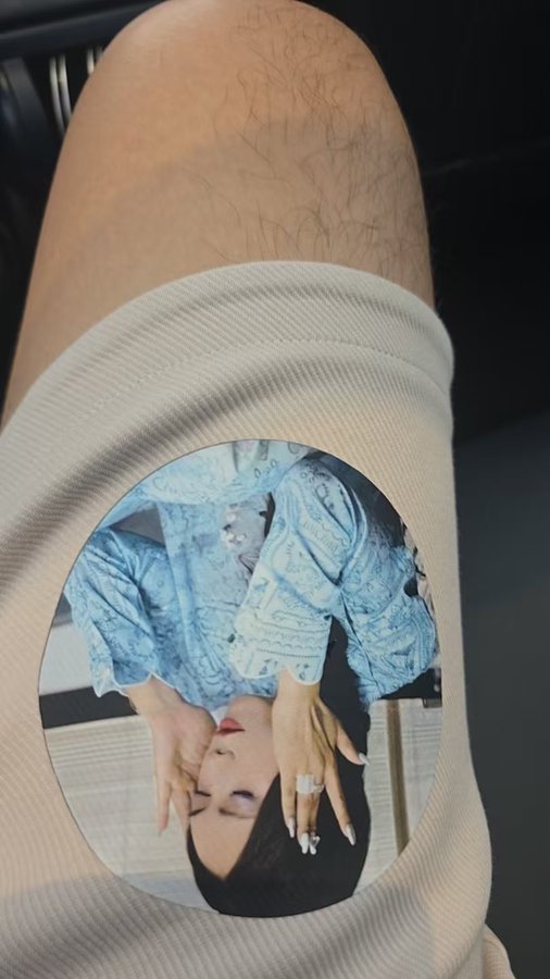 A close-up shows a person's leg wearing a circular printed sticker featuring an upside-down image of a woman in a blue denim outfit.