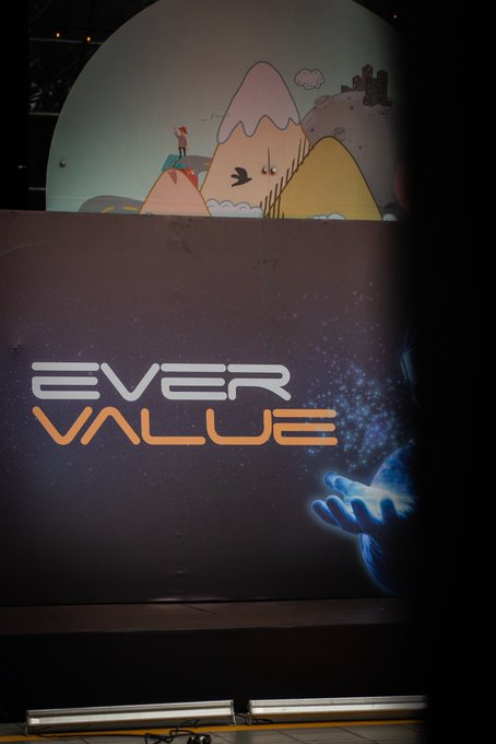 Large display screen showing 'EVER VALUE' logo with a glowing blue hand reaching toward a starry cosmic background, with a cartoon mountain landscape illustration visible above.