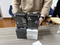 The image shows a person holding up several stacks of black and white DVDs, likely containing movies or other digital content. The person appears to be in a room with chairs and a dining table. The post seems to be related to Bitcoin or self-custody, possibly discussing the importance of hands-on experience for students in understanding complex concepts like Bitcoin.