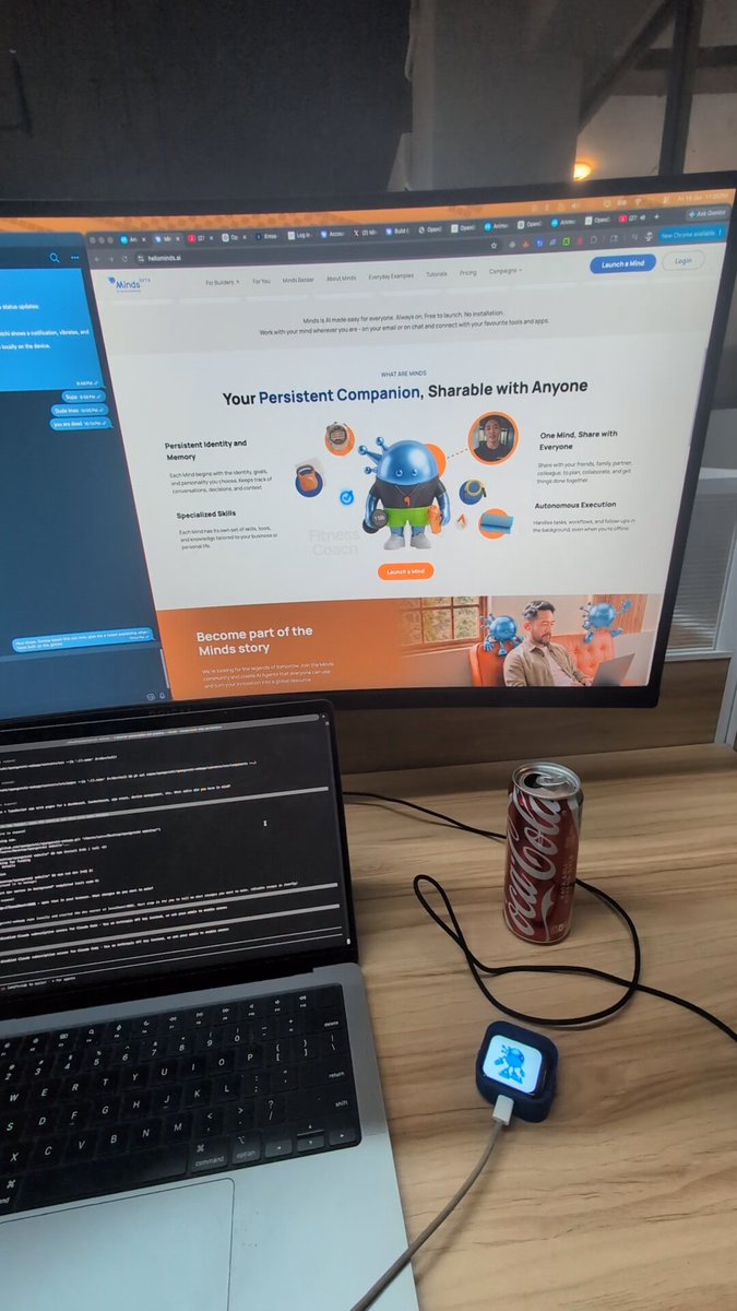 The image features a laptop computer sitting on top of a wooden desk, along with a can of soda next to it. The laptop screen displays an open web browser, possibly showing a website or application related to @hellominds agents. A small device is also present in front of the laptop, which could be used for controlling the gaming experience.