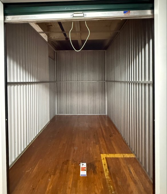 The empty interior of a storage container or truck trailer with corrugated metal walls, wooden flooring, a hanging cord, and a small sticker on the floor.