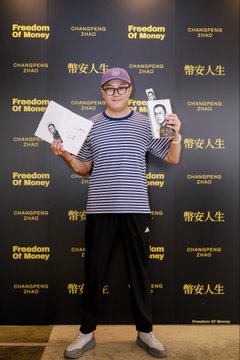 A man in a striped shirt and beanie poses at a "Freedom Of Money / Changpeng Zhao" backdrop, proudly holding up two copies of the book "幣安人生" (Binance Life). This image illustrates the social media post where the author reflects on collecting both a PDF and a physical copy of the book.