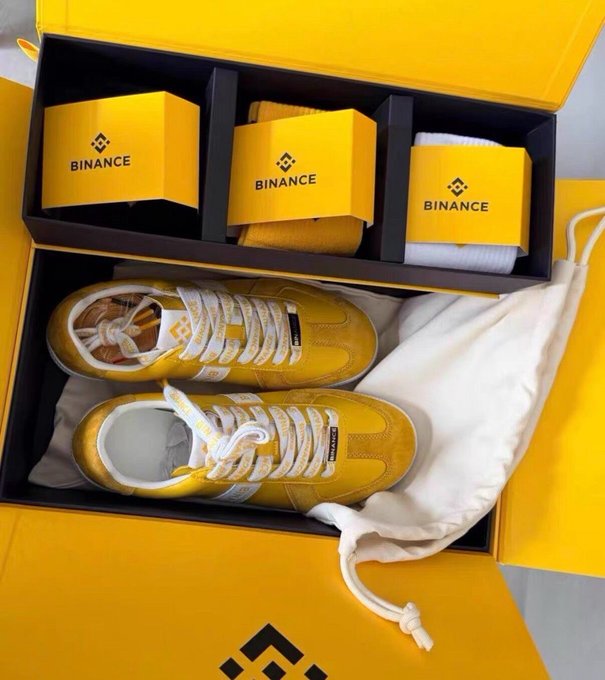 A pair of yellow sneakers and socks displayed in branded "BINANCE" boxes, serving as promotional giveaway prizes from a Rhythm BlockBeats social media contest.