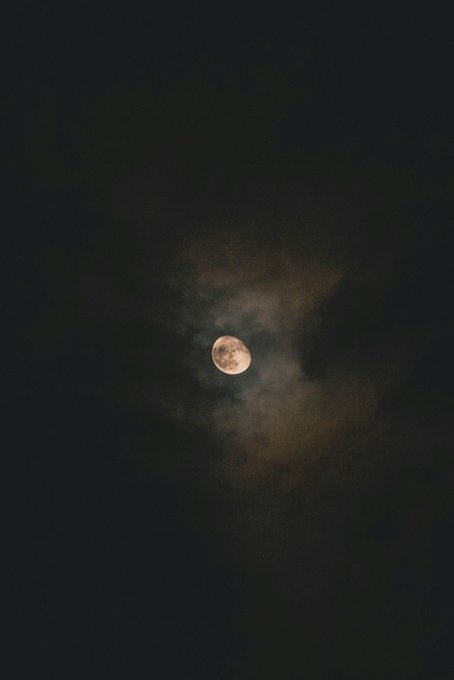 A full moon glowing orange-pink through wispy clouds in a dark night sky.
