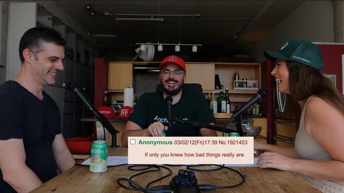The image shows three people sitting at a table with microphones, recording a podcast episode. An anonymous viewer comment reading "If only you knew how bad things really are" dated 03/02/12(Fri)17:39 No.1921453 is displayed on screen. A green ginger ale can sits on the table, and the man on the right wears a red cap, matching the post's reference to the @hellmoneypod podcast featuring hosts and guests including @rodarmor and @realizingerin.