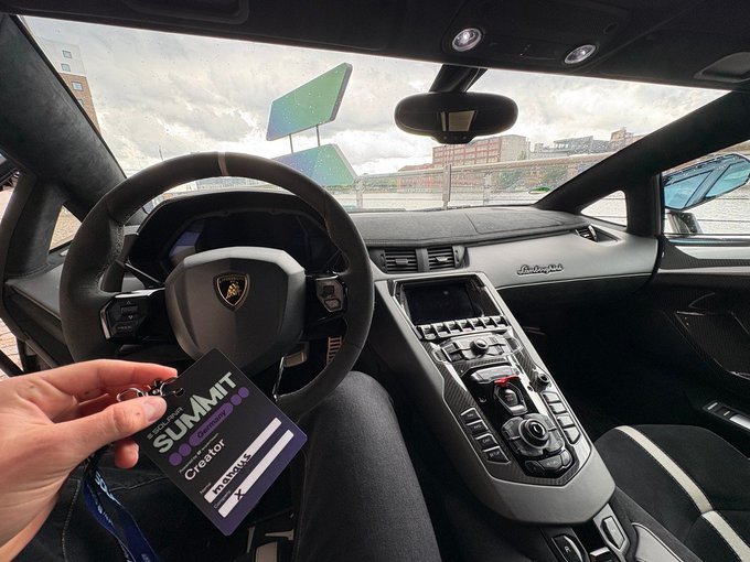 Interior view of a Lamborghini from the driver's seat, with a hand holding a 'SUMMIT Creator' lanyard in the foreground.