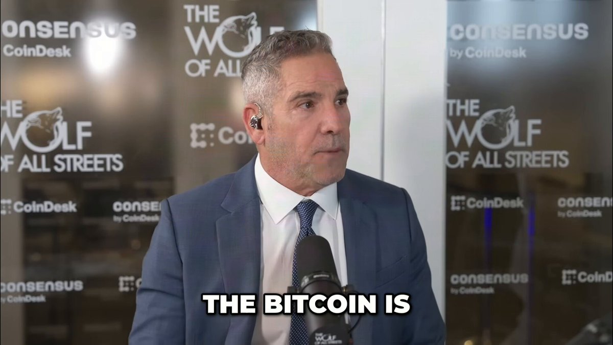 In this image, there is a man dressed in a suit talking into a microphone while sitting behind a desk. The background features text about the Bitcoin coin that says "The Bitcoin is...". There's also another person's face visible in the background who has just said "No", indicating that they are responding to what the man before them is saying. The overall atmosphere of the image suggests that it might be an interview or discussion related to Bitcoin and its value, with the first person presenting a claim about the potential worth of Bitcoins and the second person providing their response.