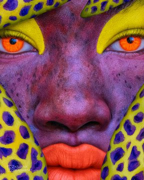 A vibrant, colorful close-up painting of a face featuring striking orange eyes, purple skin, and yellow leopard-print accents around the edges.
