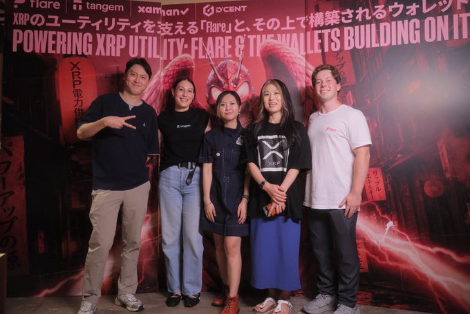 Five individuals pose in front of a vibrant red backdrop featuring Japanese text and graphics, including the logos for "Flare," "tangem," "xaman," and "D'CENT," advertising "POWERING XRP UTILITY - FLARE & THE WALLETS BUILDING ON IT." This image visually represents the successful conclusion of the side event mentioned in the accompanying post.