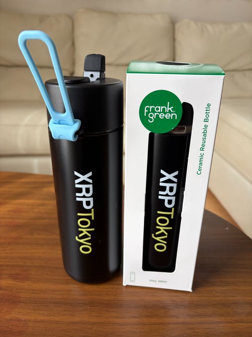 A matte black Frank Green ceramic reusable water bottle branded with "XRP TOKYO" sits beside its retail packaging on a wooden table, showcasing the XRP-branded merchandise referenced in the post about Ripple's collaboration giveaway for events.