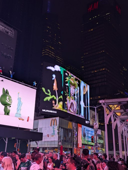 A nighttime view of a crowded Times Square with bright digital billboards, including ones for H&M and MURMEOW featuring a Medusa illustration.