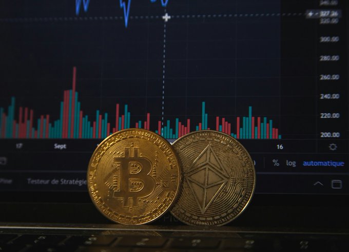 Two physical representations of cryptocurrency—a gold Bitcoin coin and a gold Ethereum coin—rest on a laptop keyboard, with a stock chart displaying price fluctuations and dates (Sept, 16) visible in the background, visually illustrating the volatility of digital currencies like the failed TerraUSD.