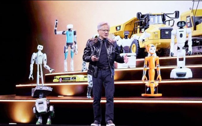 A man in a black leather jacket stands on stage surrounded by various humanoid robots and a screen showing construction vehicles.