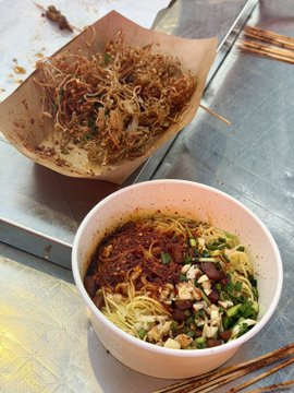 The image shows two bowls of food sitting side by side on a table. One bowl contains noodles with various toppings such as green onions and other vegetables, while the other bowl has a more plain appearance without any visible toppings or garnishments. The bowls are placed next to each other, creating an interesting contrast in their contents.