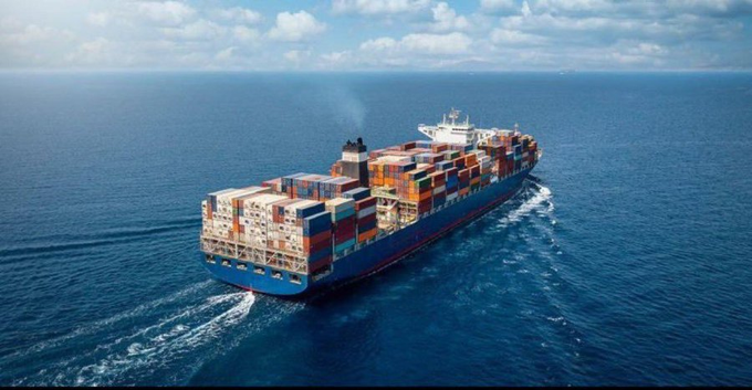 Aerial shot of a large blue container ship sailing across the open ocean loaded with colorful cargo containers.