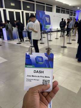 A hand holding a DASH event credential for 'José Maria de Pina Mette, Relationship Manager, ExAtlas' at what appears to be a Dash cryptocurrency conference.